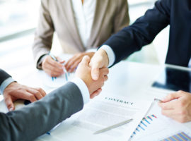 Image of business partners handshaking over business objects on workplace